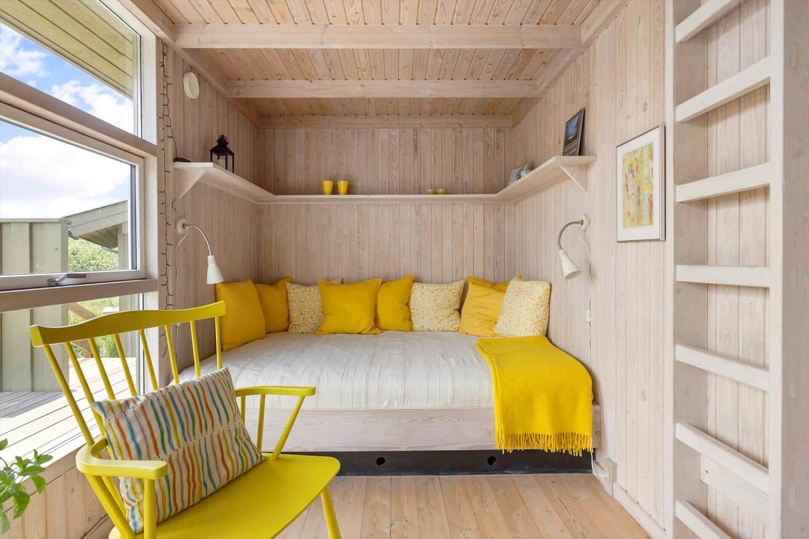 Ein Schlafzimmer mit gelber Couch und Stuhl. Holzwände und Fenster mit Blick.