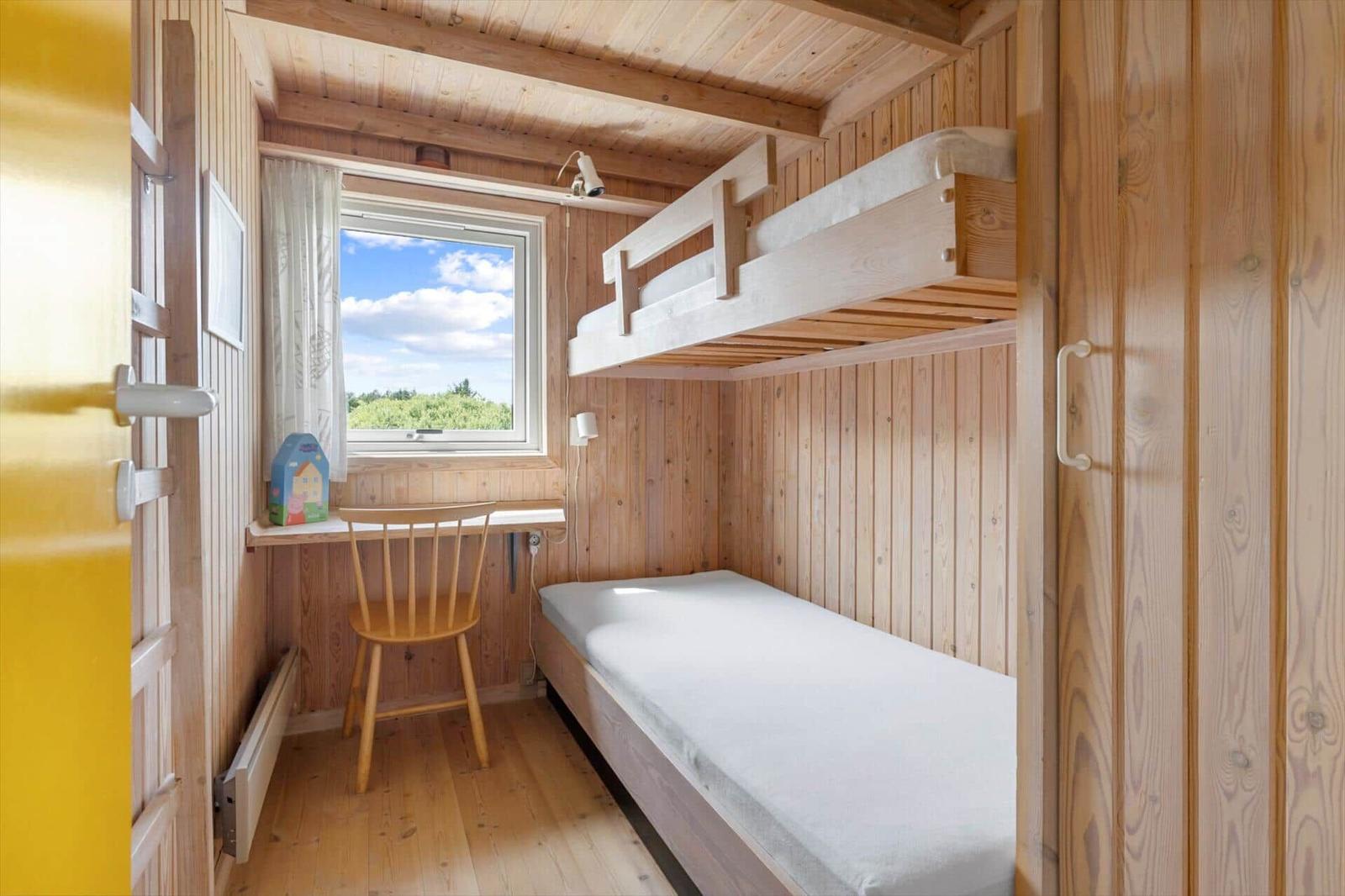 Zimmer mit Doppelstockbett, Schreibtisch und Fenster mit Blick auf Grün.