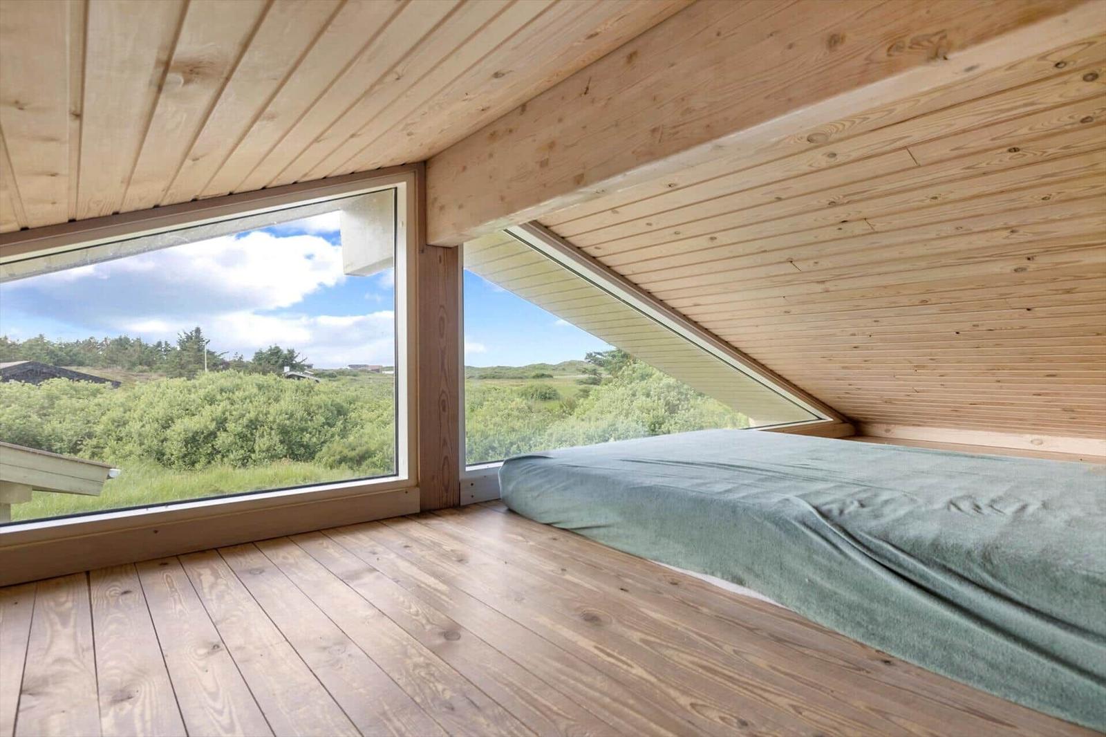 Schlafzimmer mit Holzdecke und -boden, großes Fenster mit Blick auf Grünland.
