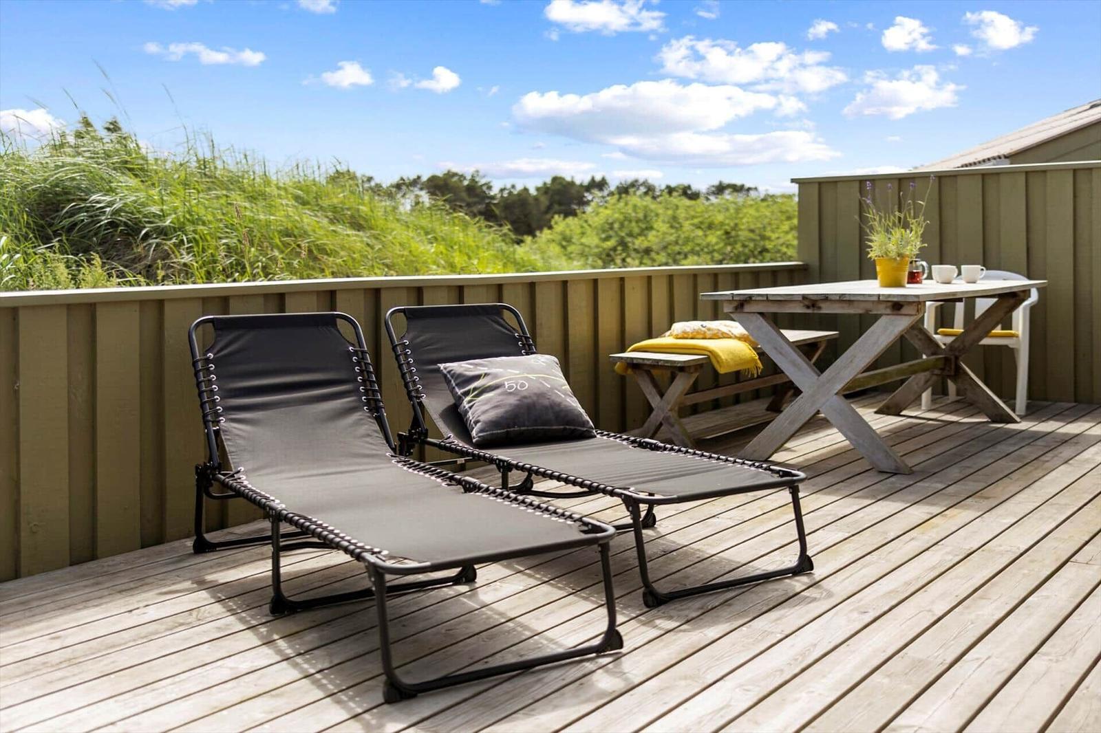 Terrasse mit zwei Liegestühlen, Tisch und Blick auf Grünflächen.