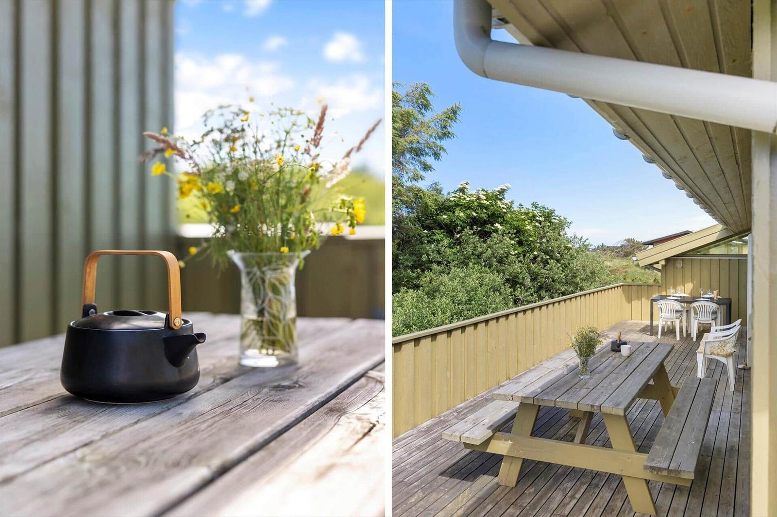 Holztisch mit Teekanne und Blumen auf Terrasse mit Blick auf Grünflächen