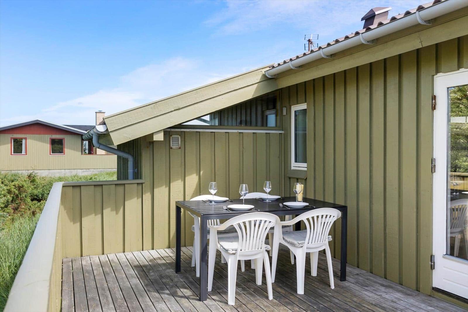 Terrasse mit Tisch und Stühlen an einem Haus mit Holzwand und Dachüberhang.