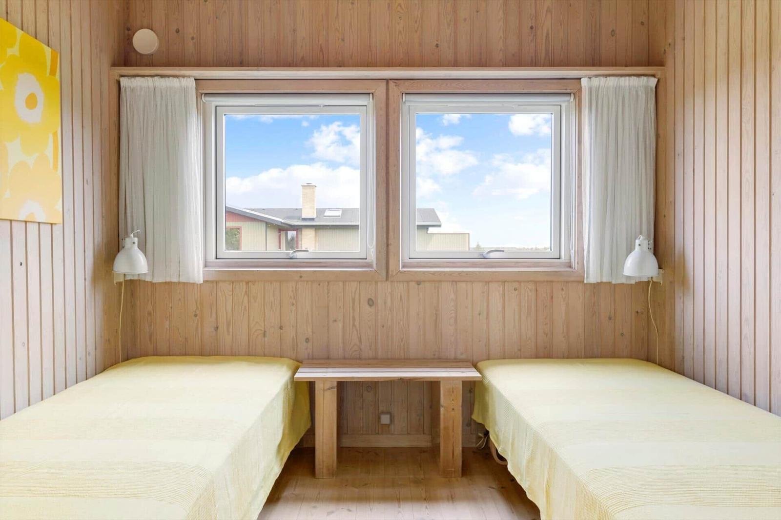 Zwei Einzelbetten mit gelben Bettwäschen stehen unter einem Fenster mit Blick auf ein Haus.