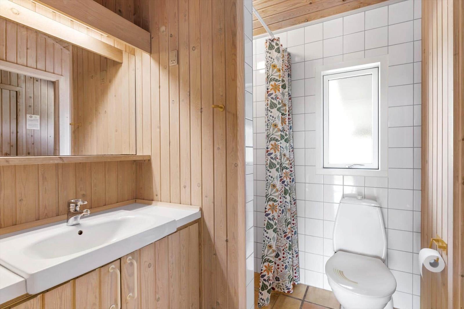 Badezimmer mit Waschbecken, Spiegel, Toilette und Dusche mit floraler Vorhang.