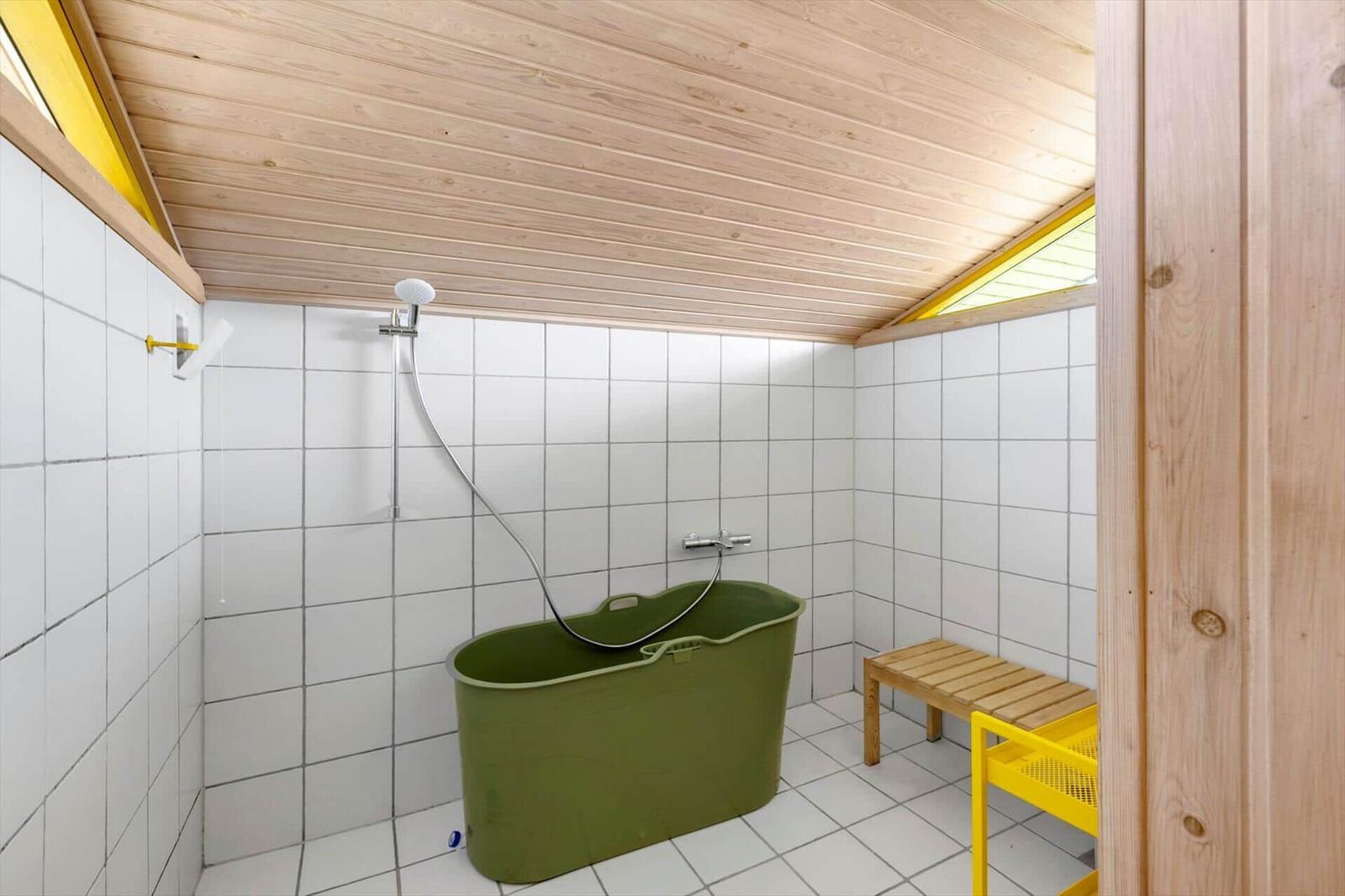 Dusche mit grünem Badewannenfass, Holzdecke und gelben Akzenten.