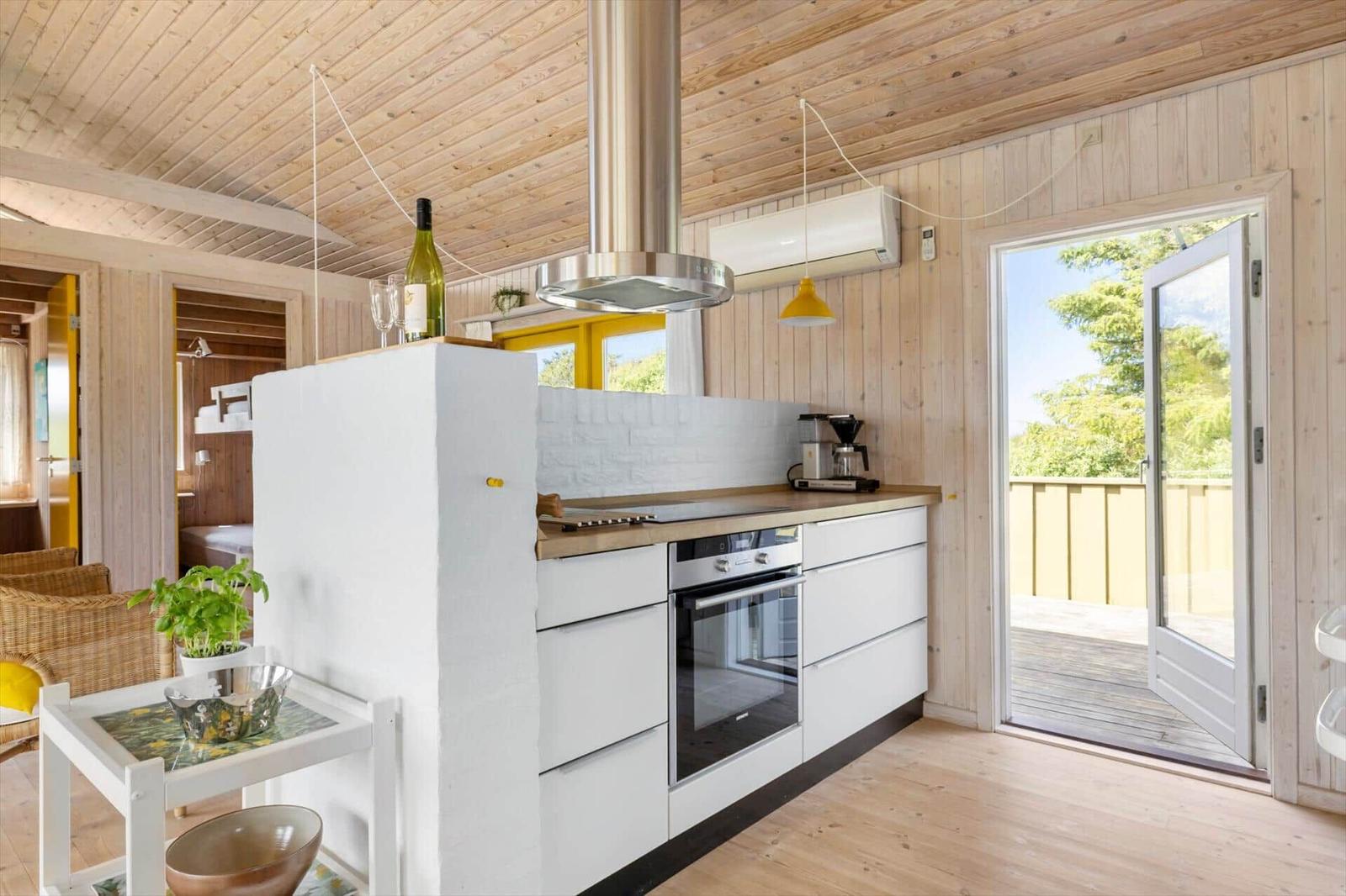 Küche mit weißer Einbauküche, Holzwand und Terrassentür.