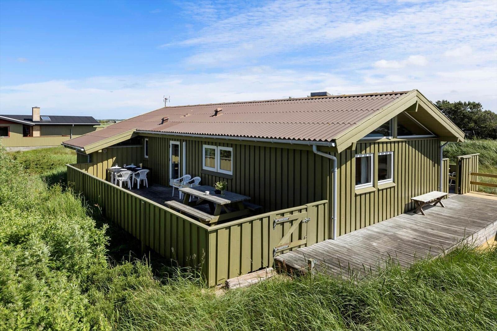 Grünes Ferienhaus mit Terrasse und Holzdecke. Außentisch, Stühle und Garten.