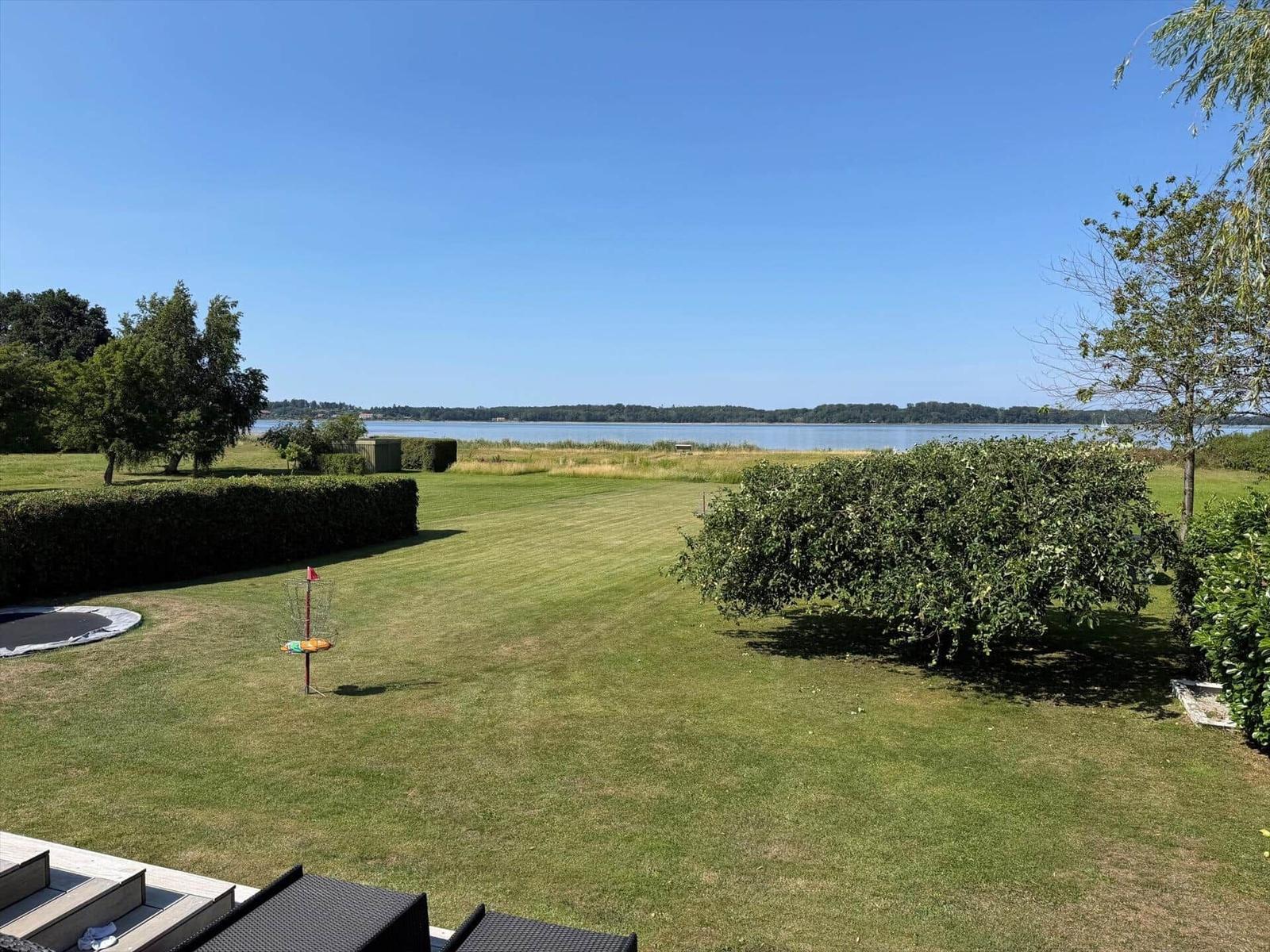 Großer Garten mit Blick auf See und Bäume. Trampolin und Discgolf-Target sichtbar.