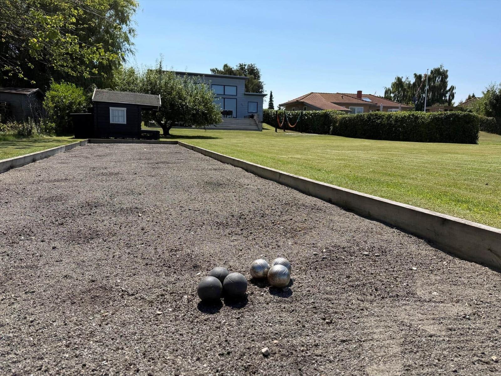 Pétanque-B场地 mit Bällen, Grasfläche und Haus im Hintergrund.