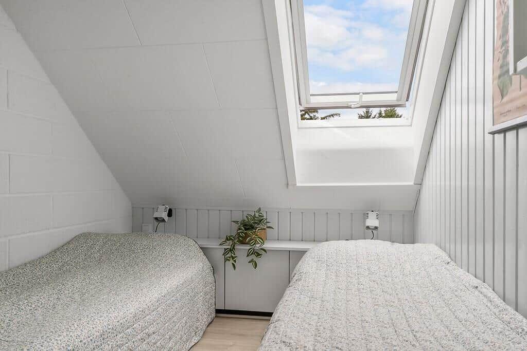 Two beds under sloped ceiling with skylight and plant.