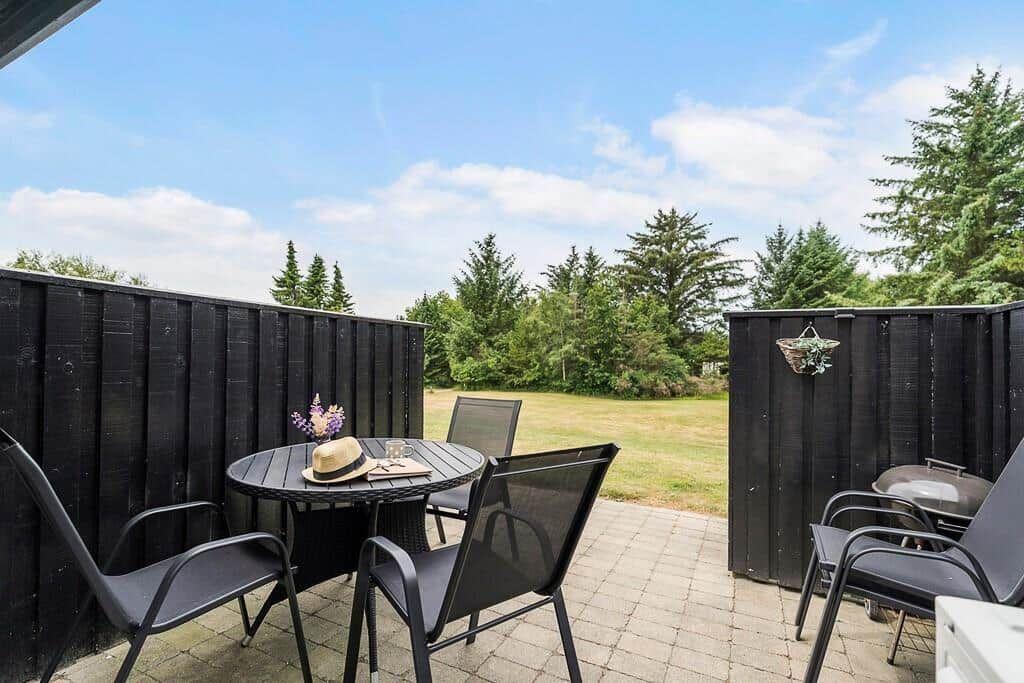 Terrace with table, chairs, and grill. View of green lawn and trees.