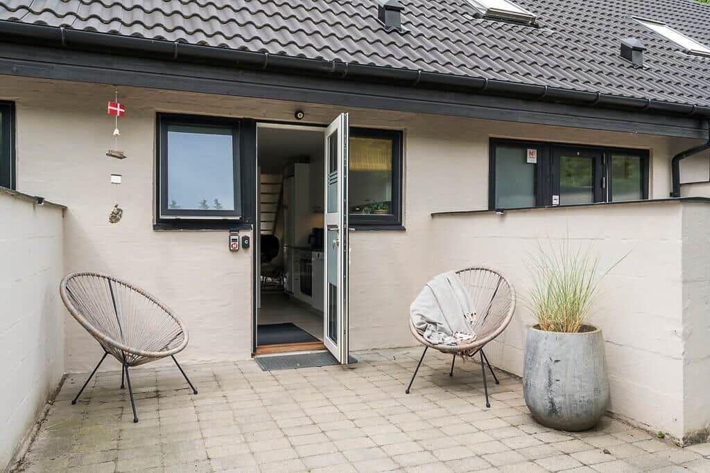 Backyard with two chairs, a plant, and an open door to the house.