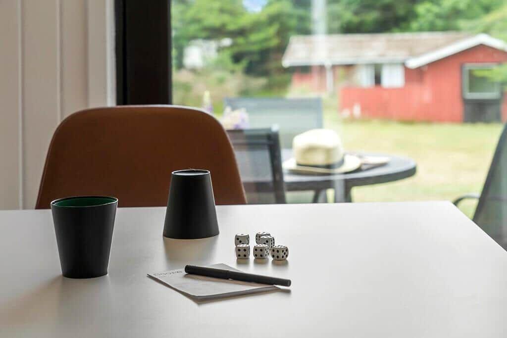 Table with dice, cup, and pen in front of window with garden view.