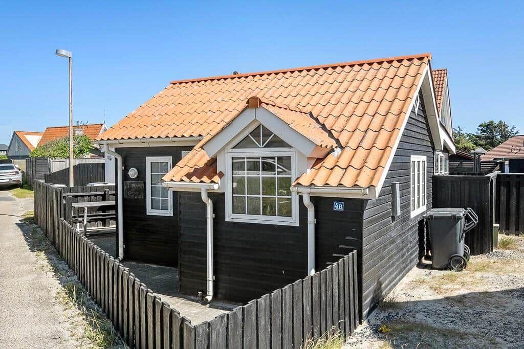 Black wooden house with red tiled roof and white-framed windows behind wooden fence.