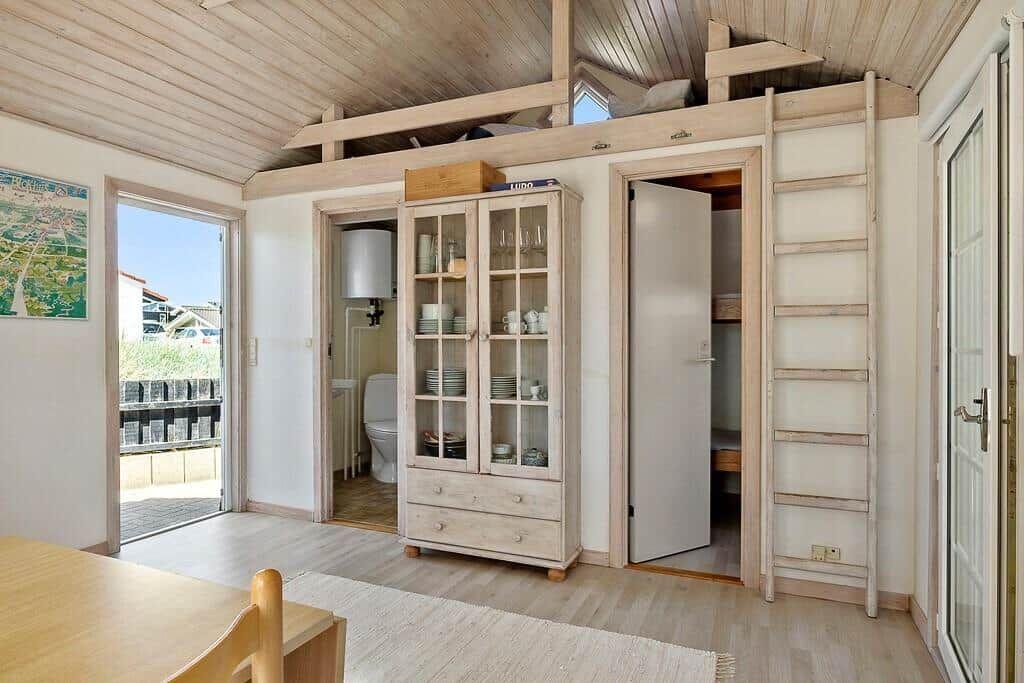 Living area with dining space, cabinet, toilet, and loft area with ladder.
