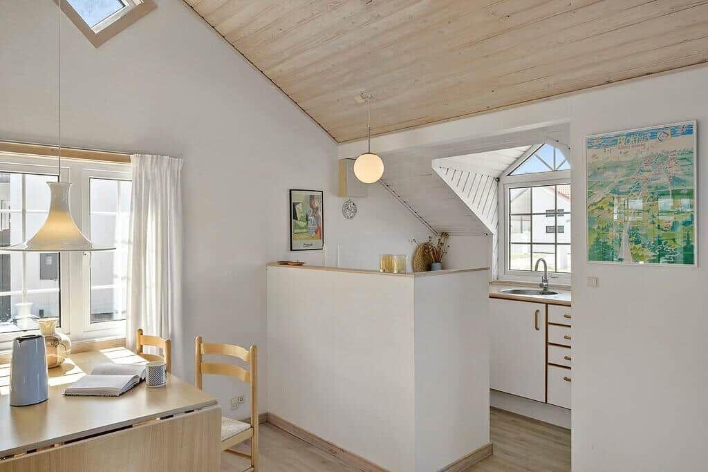 Kitchen with dining area under wooden ceiling, windows, wall art, and kitchen counter.