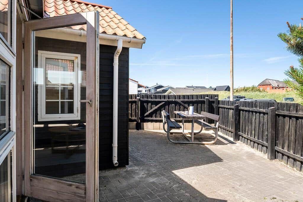 Terrace with table and benches, surrounded by wooden railing and view of houses.