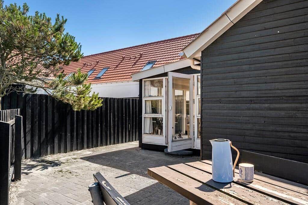 Terrace with table, kettle, and mug. Backyard with wooden wall and window.