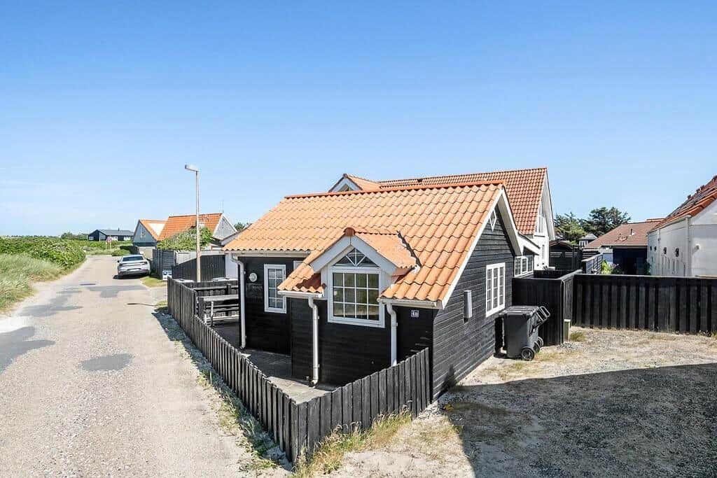A small house with a red roof and black facade stands on a road.