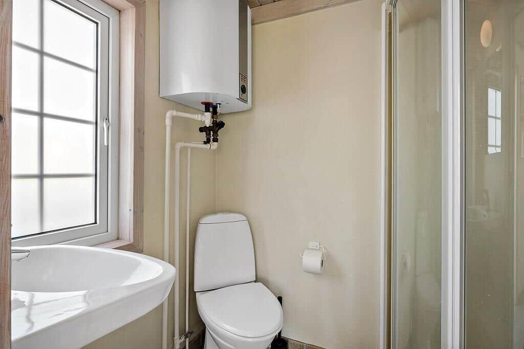 Bathroom with toilet, shower, and sink under window.