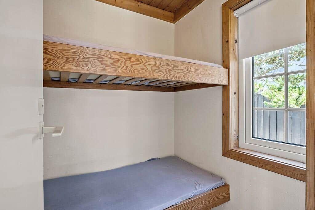 Room with bunk bed and window with wooden frame.