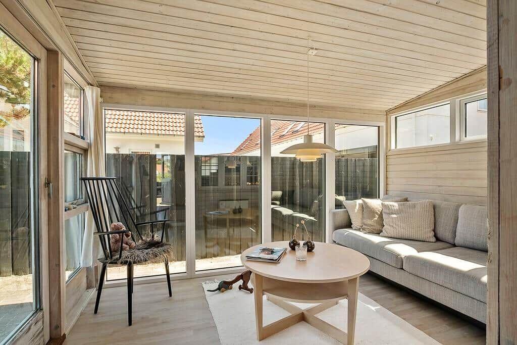 Living area with sofa, table, and chair. Large windows offer view of the garden.