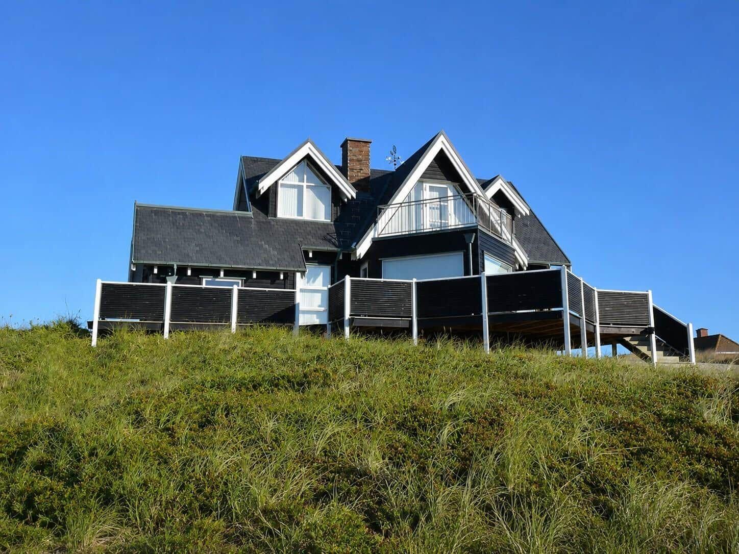 Schwarzes Haus mit Balkon auf grüner Anhöhe unter blauem Himmel