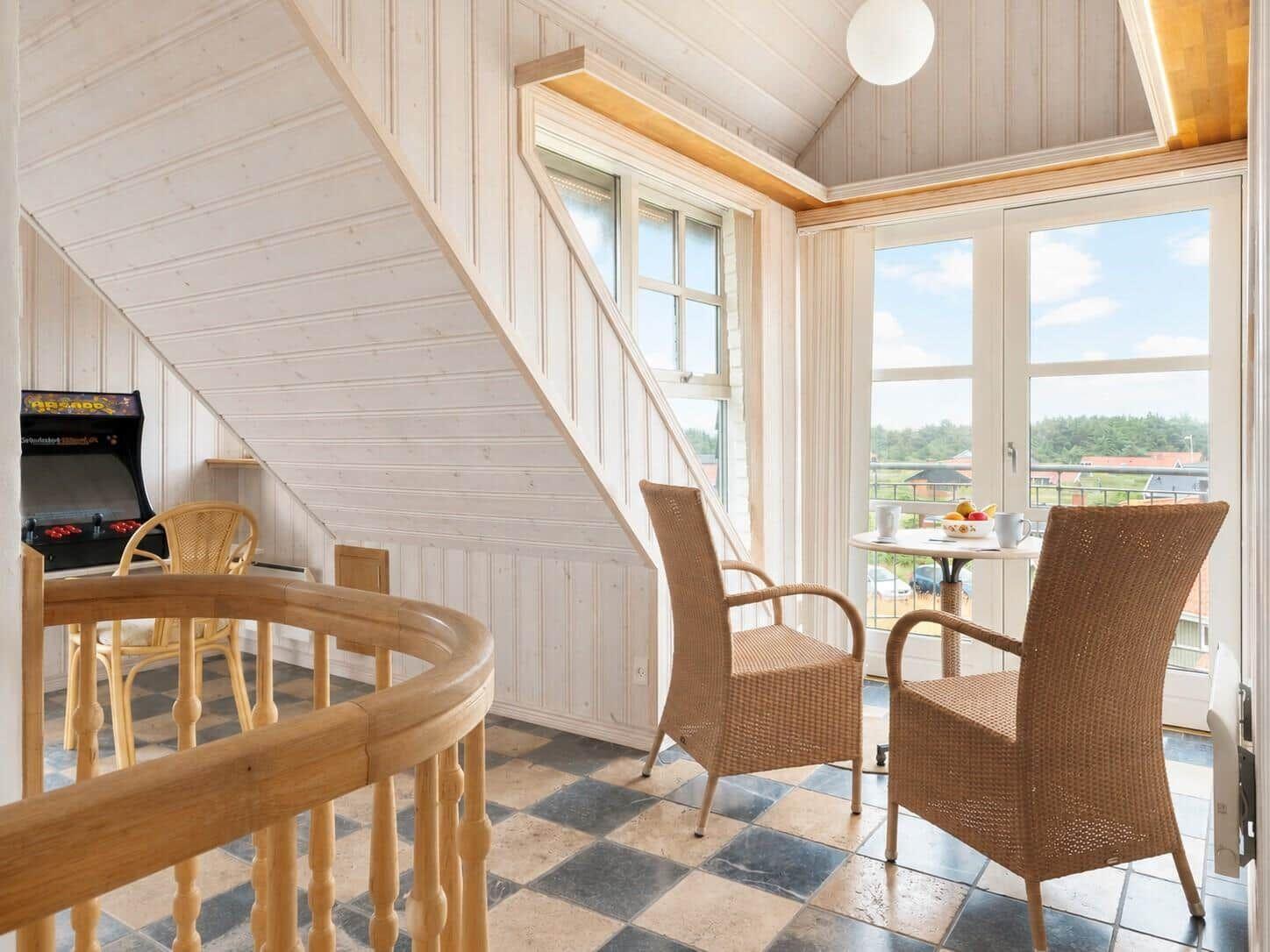 Raum mit Treppe, Sitzgelegenheit und Arcade-Spiel. Blick auf Balkon mit Tisch und Stühlen.