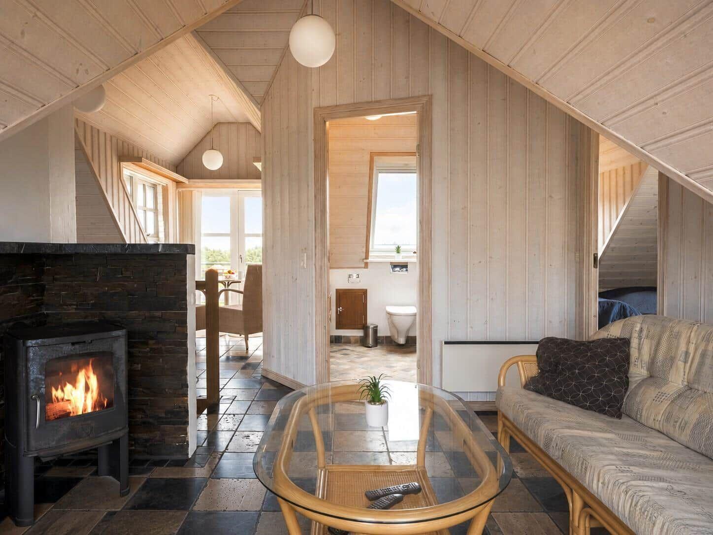 Wohnraum mit Kamin, Glas-Tisch und Sofa. Im Hintergrund ist die Toilette sichtbar.
