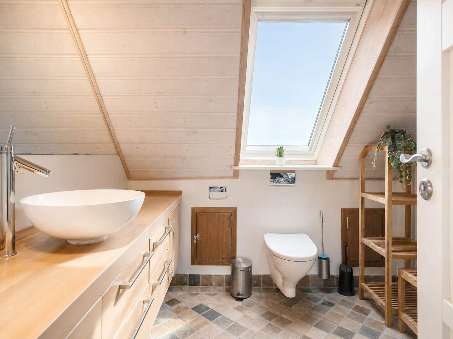 Badezimmer mit Dachschrägen, Waschtisch und Toilette unter Dachfenster.