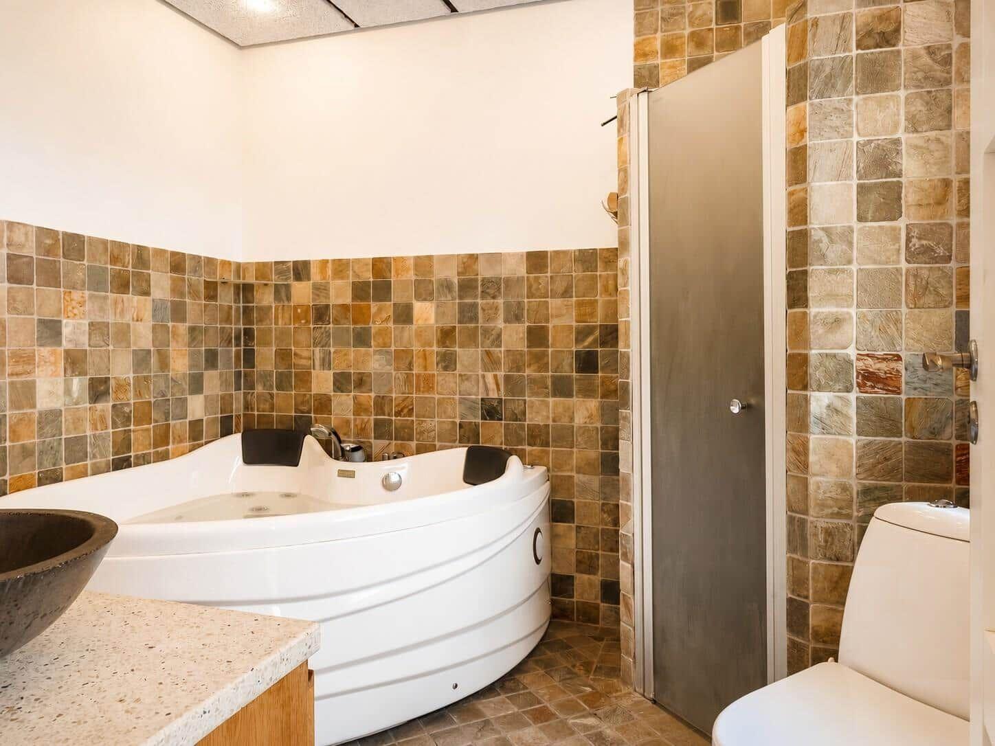Bad mit Whirlpool, Toilette und Dusche mit Steinfliesenwand.