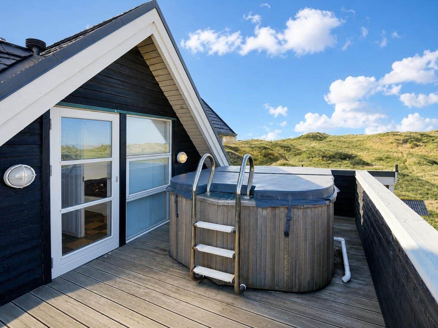 Haus mit Whirlpool auf Terrasse, Blick auf grüne Dünen.