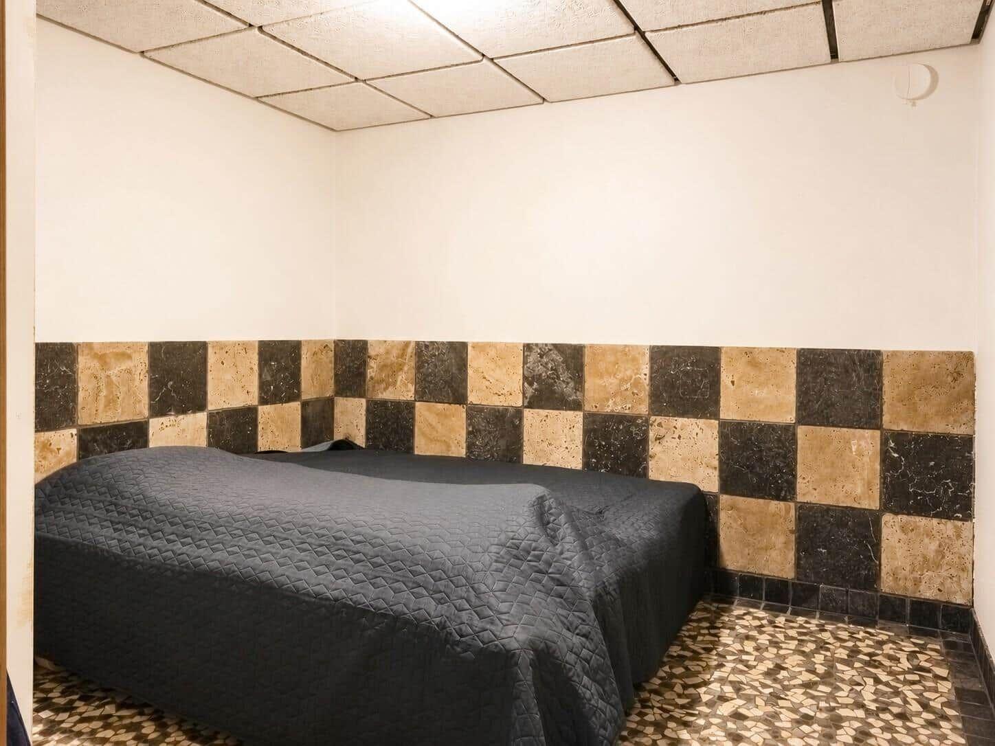 Schlafzimmer mit Bett, schwarz-weißem Boden und gemustertem Wandpaneel.