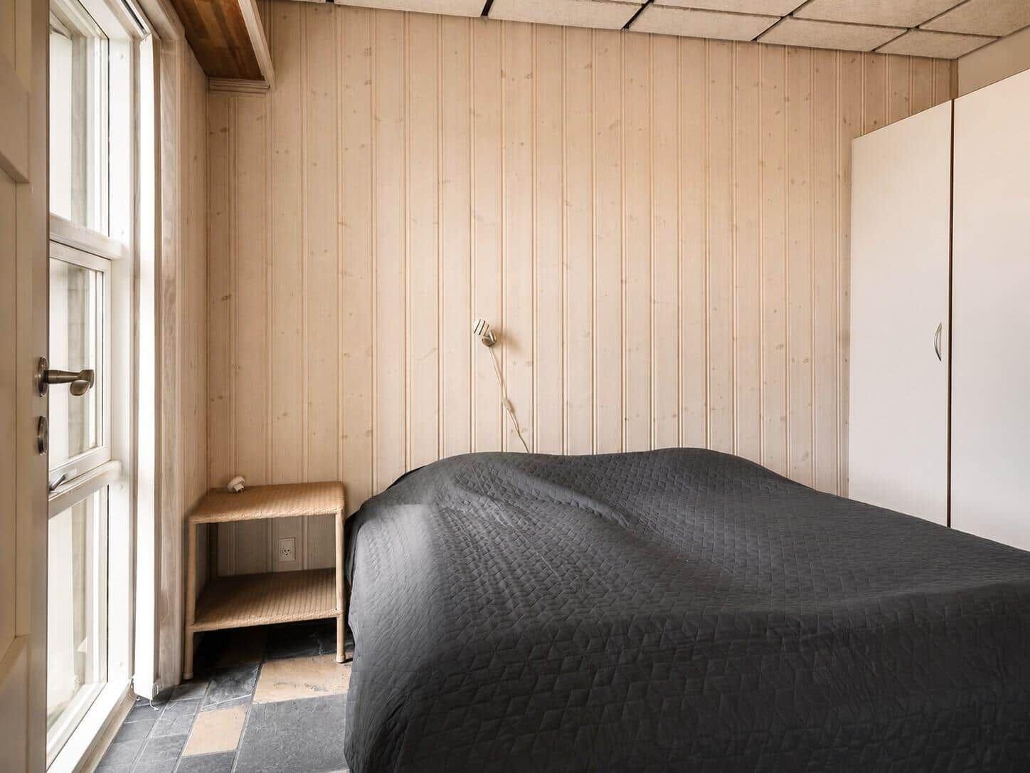 Schlafzimmer mit Holzwand, Bett, Kleiderschrank und Fenster.