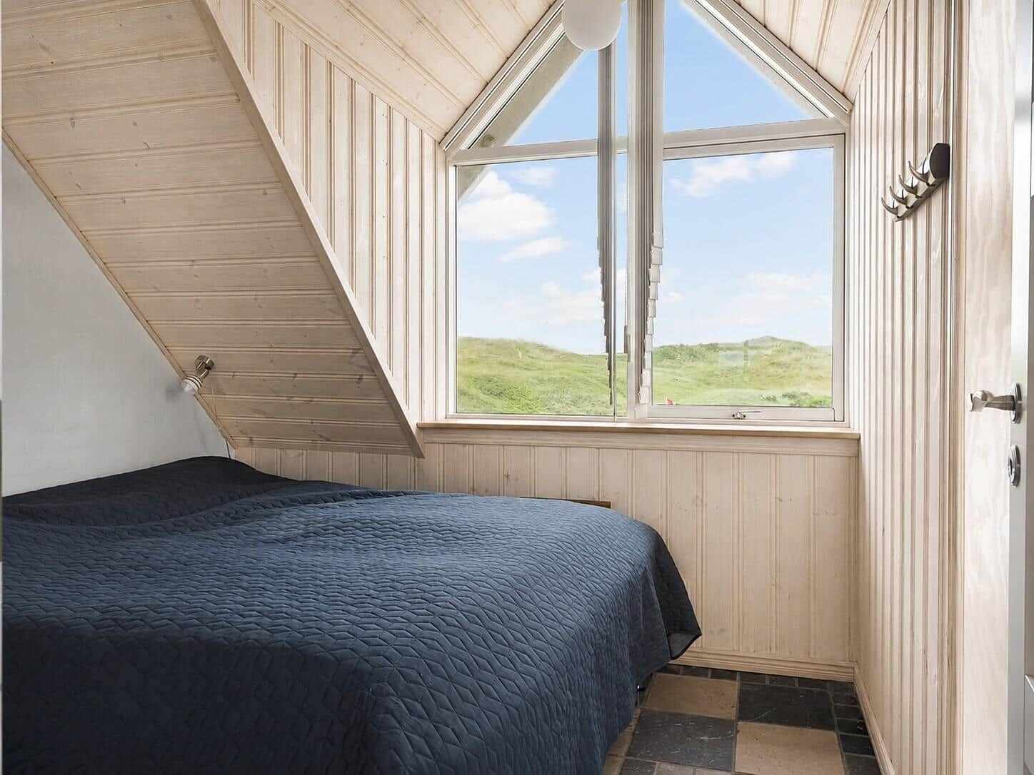 Schlafzimmer mit Dachschrägen, großem Fenster und Blick auf Grünland.
