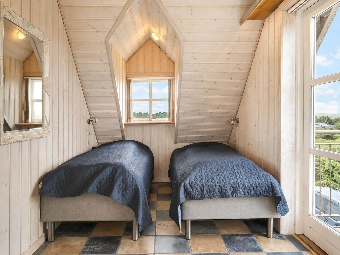 Zwei Betten in einem Dachzimmer mit Holzwänden und Fenstern.
