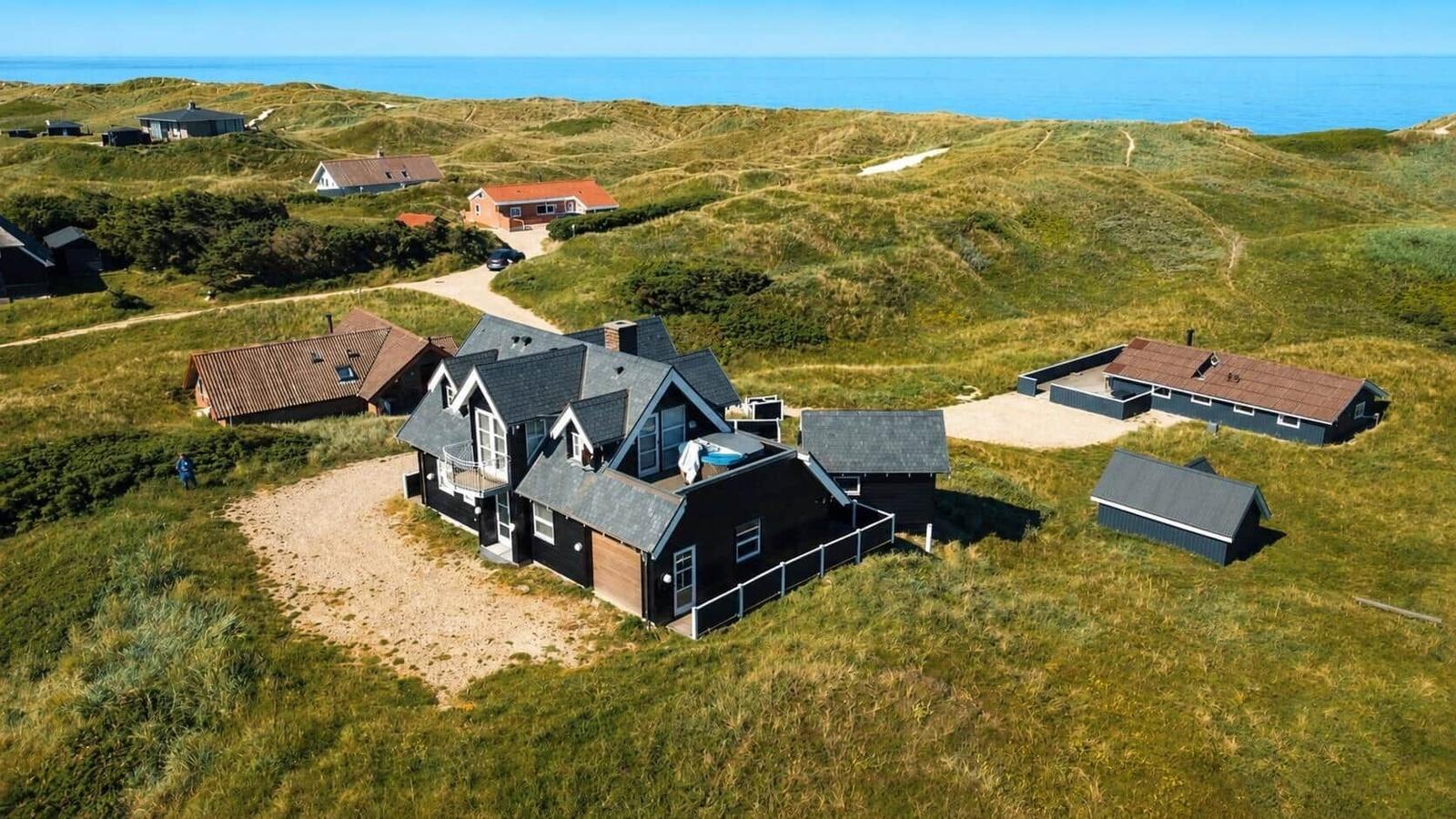 Haus mit Pool und Terrasse auf grüner Dünenlandschaft mit Blick auf das Meer.
