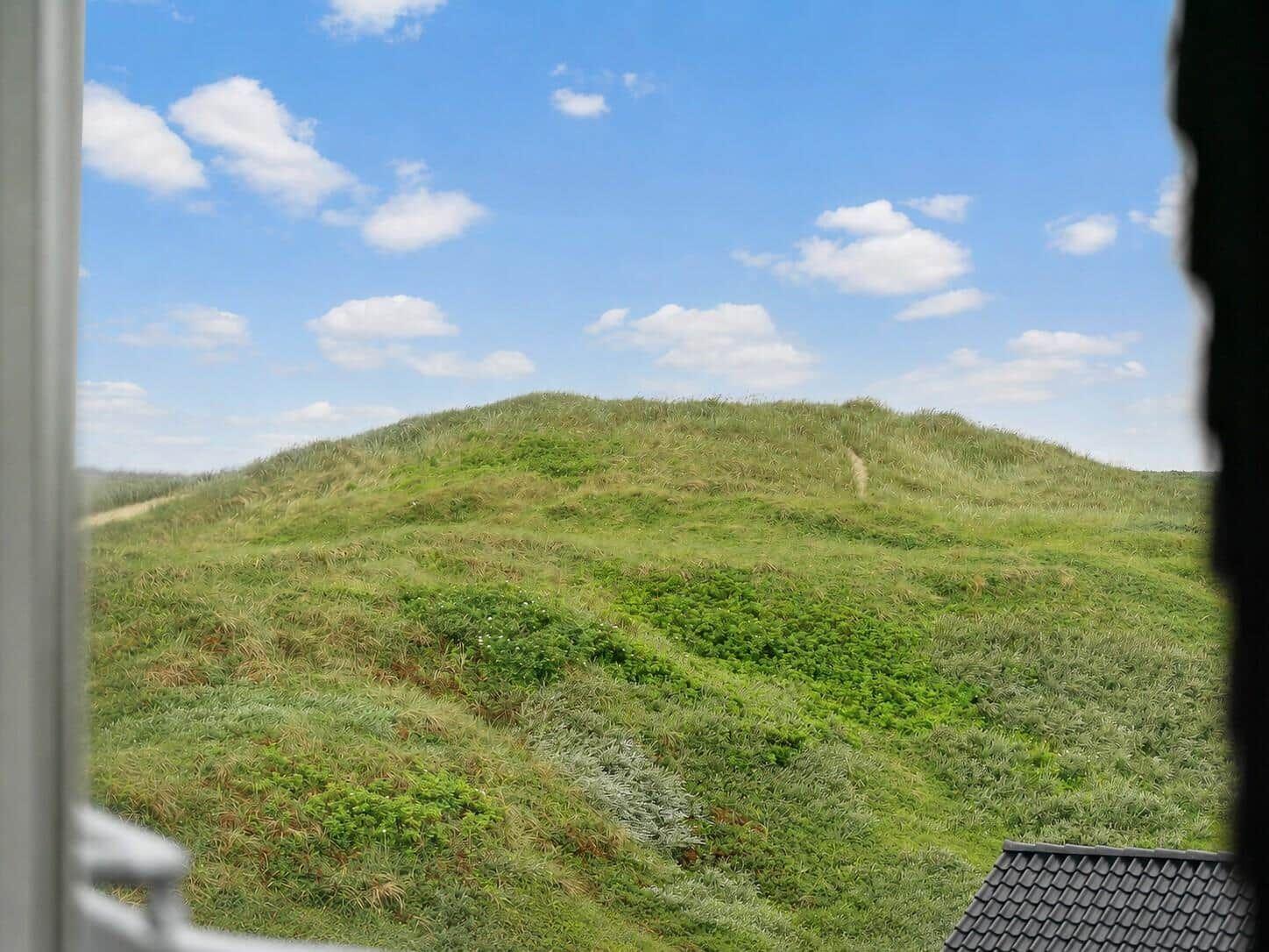 Grüne Dünen unter blauem Himmel mit weißen Wolken. Blick aus dem Fenster.