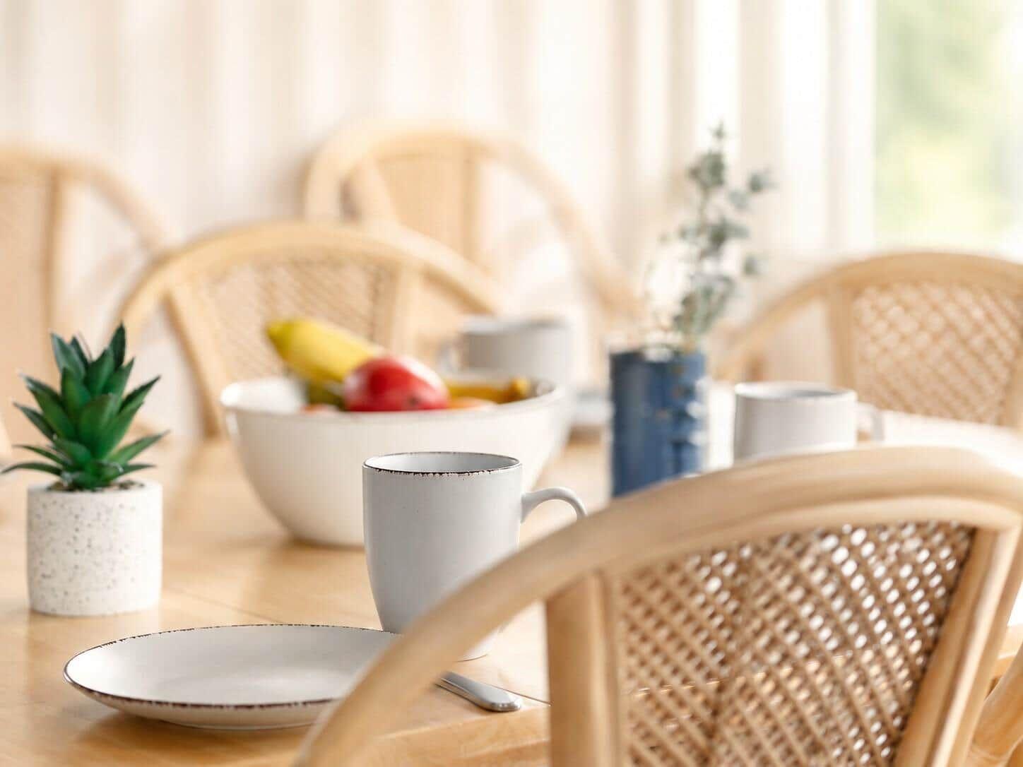 Esstisch mit Stühlen, Teller, Tasse und Obstschale.