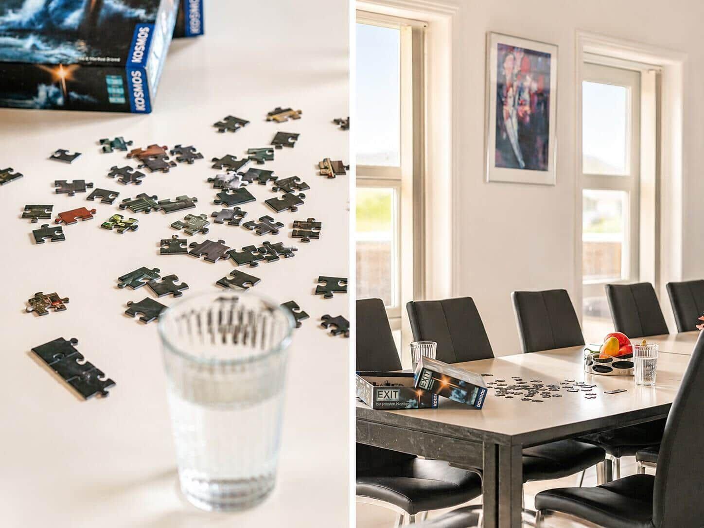 Tisch mit Puzzlestücken und Glas Wasser. Esszimmer mit Tisch, Stühlen und Fenstern.