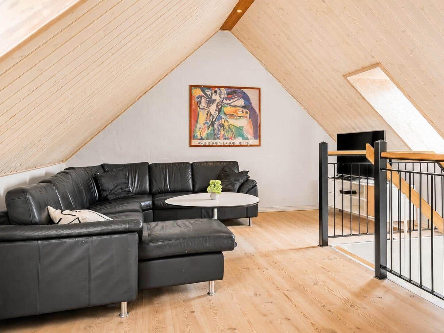 Schwarzes Ledersofa unter Holzdach mit Wandbild und runder Tisch