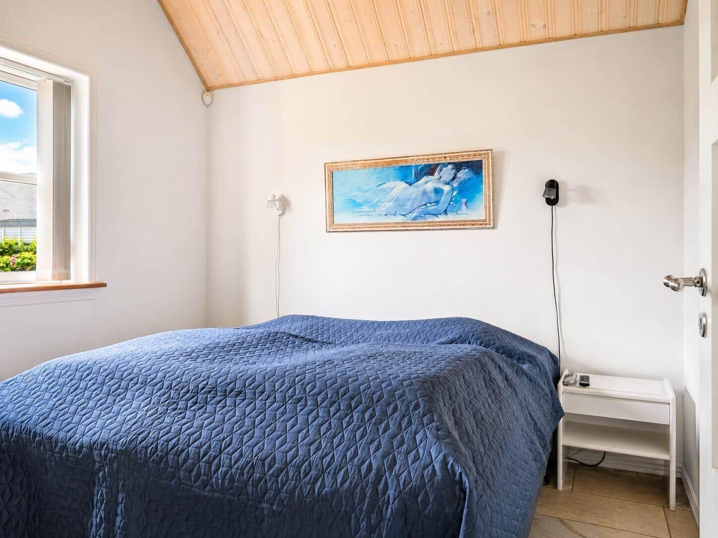 Schlafzimmer mit blauem Bett, Fenster und Wandbild.