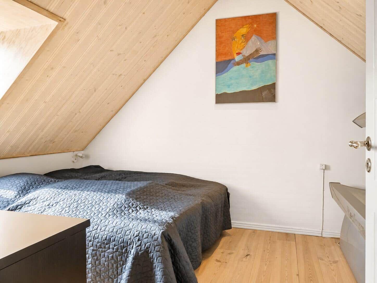 Schlafzimmer mit Dachschrägen, Bett und Wandbild.