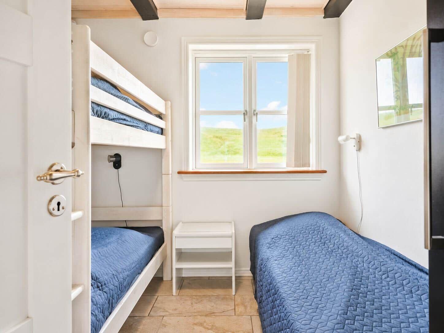 Schlafzimmer mit Doppelbett und Etagenbett, Fenster mit Blick auf Grünfläche.