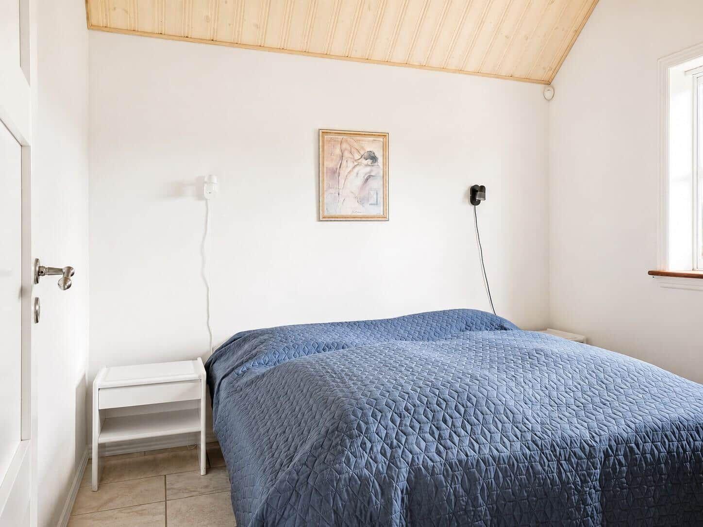 Schlafzimmer mit Bett, Nachttisch und Wandbild. Holzdecke und Fenster.