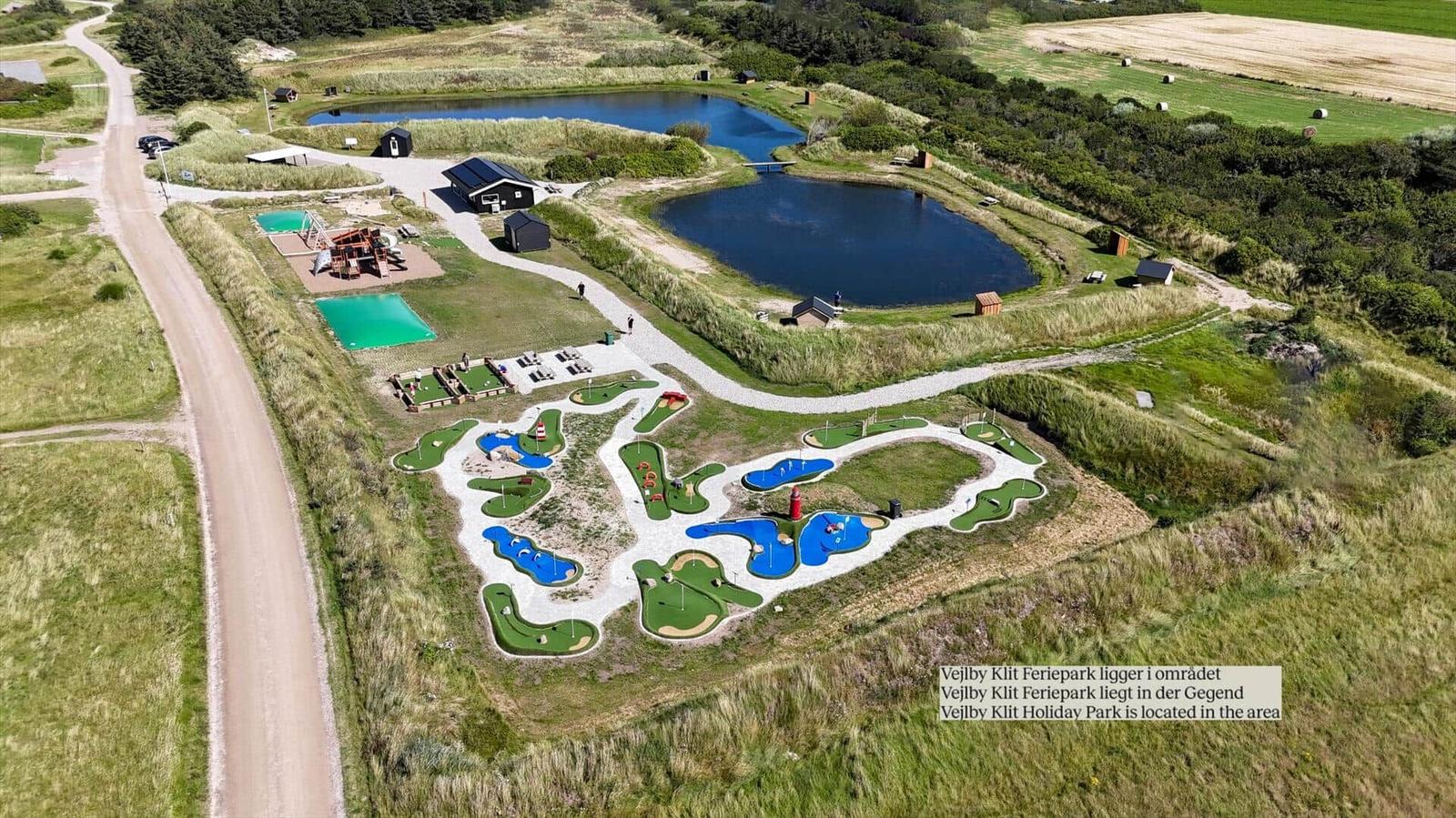 Aerial view of Vejlby Klit Holiday Park with mini-golf, ponds, and surrounding green fields.