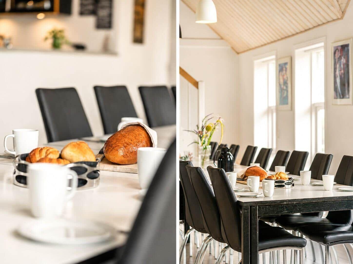 Esszimmer mit langem Tisch, schwarzen Stühlen und Brot. Holzdecke und Fenster sorgen für Licht.