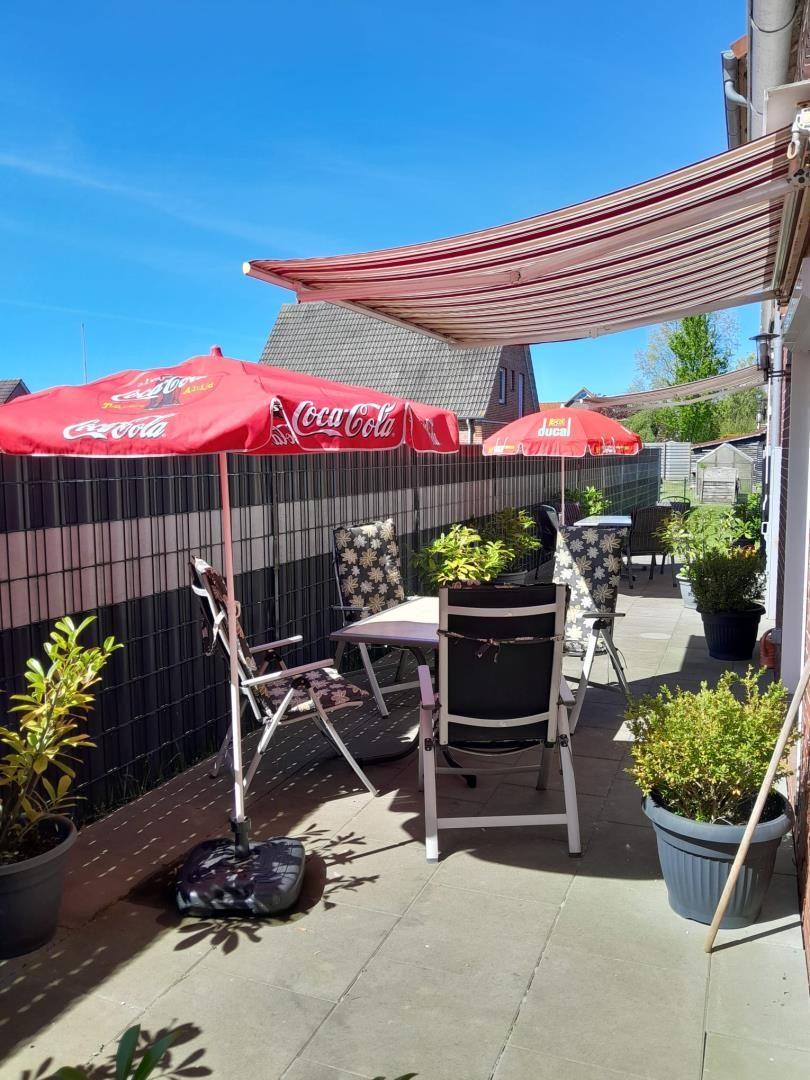 Terrasse mit Tisch, Stühlen, Sonnenschirmen und Pflanzen unter einem Markisenüberdachung.