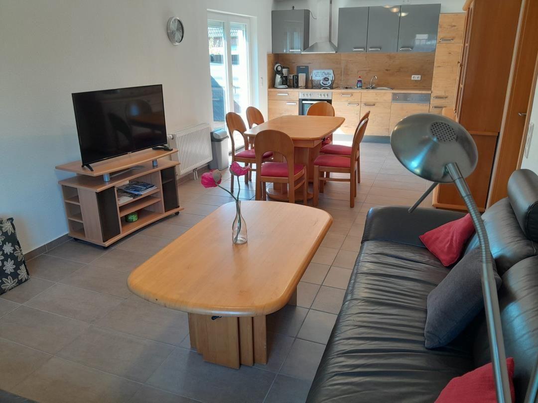 Wohn- und Essbereich mit Sofa, Esstisch und Küche im Hintergrund.