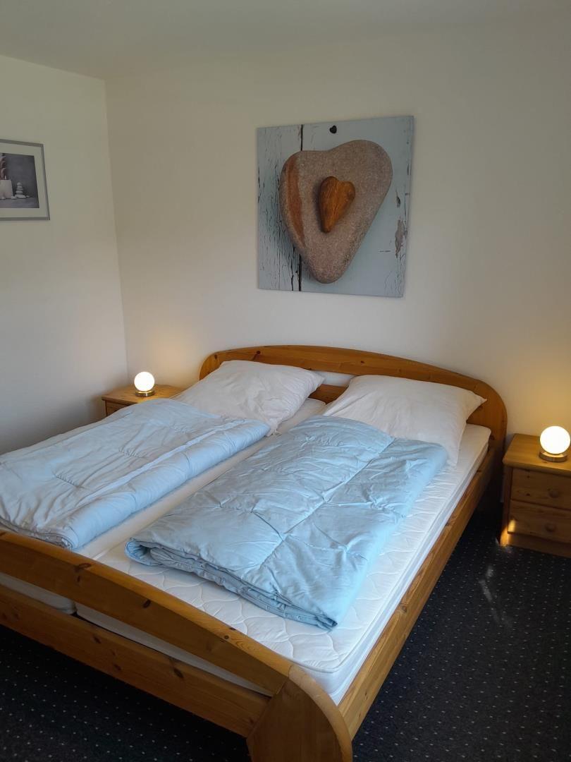 Schlafzimmer mit Holzbett, zwei Nachttischen und Wandbild mit Herz